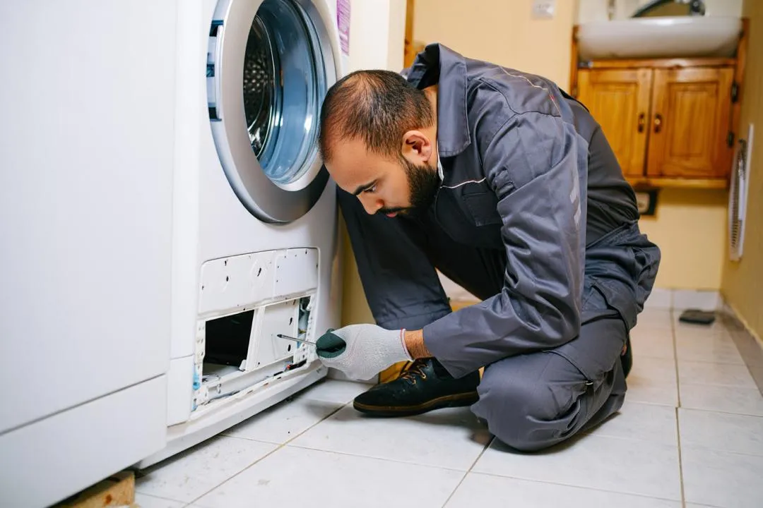 تصویر تعمیرکار تعمیرات لباسشویی در مشهد در حال تعویض فیلتر تخلیه ماشین لباسشویی است.